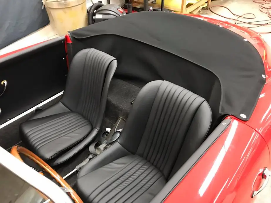 A red roadster with black pleated seats and a new black top boot.