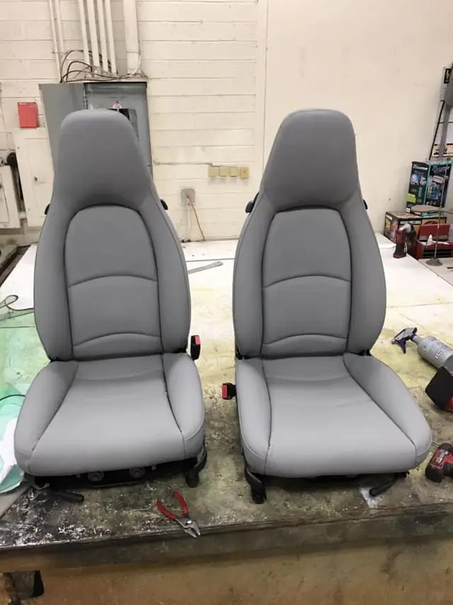 A pair of newly reupholstered gray fabric seats, on the workbench.