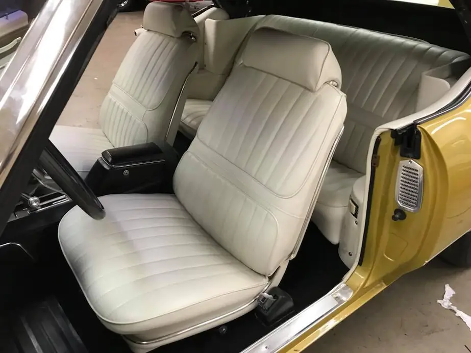 A vintage muscle car in yellow with a black vinyl top and a fresh white pleated interior restoration.